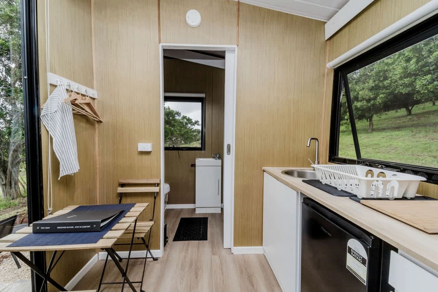 A compact kitchenette with a sink, a small window, and a view of greenery outside.