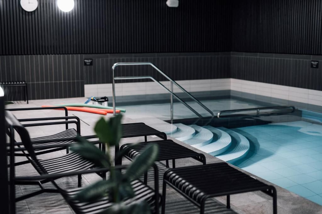 Un espace piscine avec des marches menant à l’eau, une échelle et des chaises en métal noir.