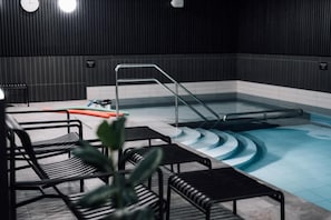 Un espace piscine avec des marches menant à l’eau, une échelle et des chaises en métal noir.