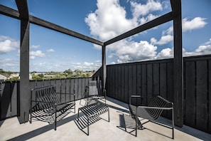 Une terrasse extérieure avec des chaises en métal et un sol en béton, donnant sur un quartier résidentiel.