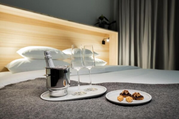 Un lit bien fait, avec une tête de lit en bois, une table de chevet sur laquelle se trouvent une bouteille et des verres, et une assiette remplie de biscuits.