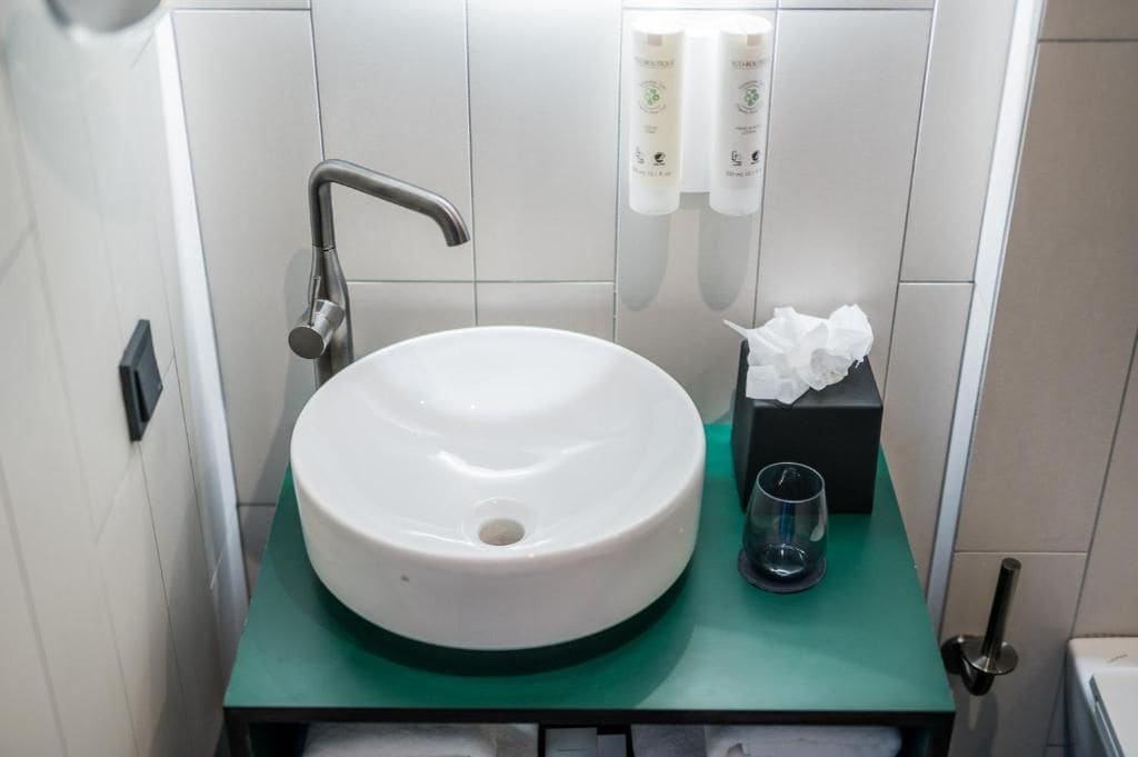 Un baño con lavamanos blanco, encimera verde, una caja de pañuelos y un vaso.