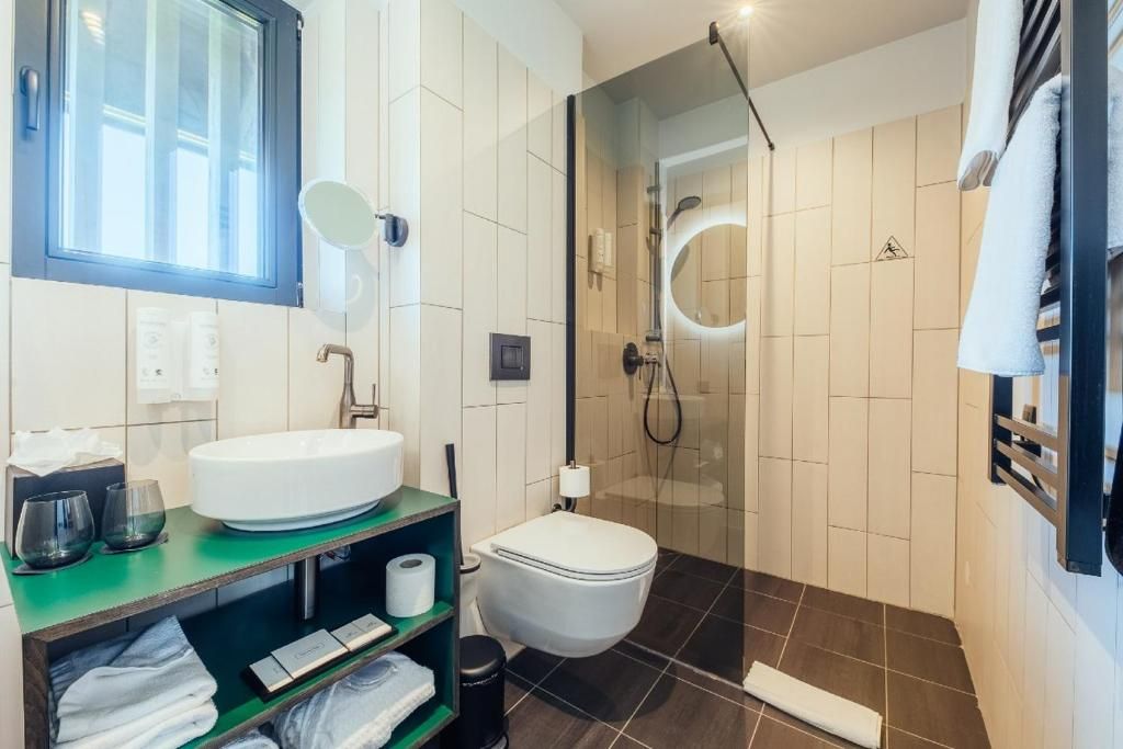 Een moderne badkamer met een ruime witte wastafel, een toilet, een douche met glazen wanden en een groene badkamerkast met handdoeken.
