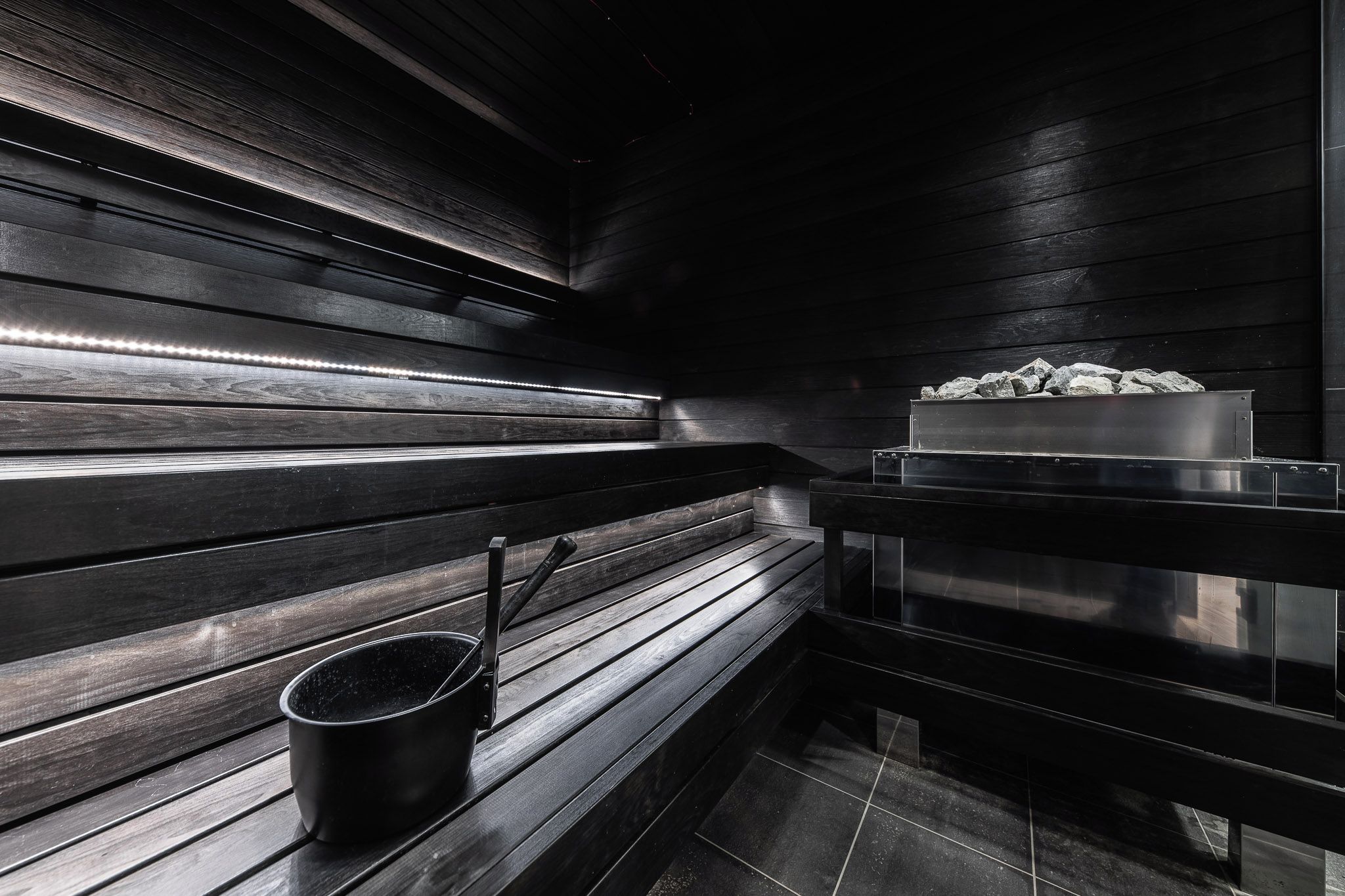 Una sauna con bancos de madera, un cubo de metal y un recipiente con piedras.