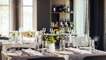 A restaurant setting with tables set for dining, featuring clear glassware and a vase with green foliage.