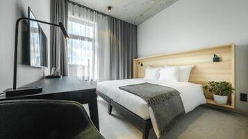 A modern hotel room with a bed, desk, chair, and a potted plant.