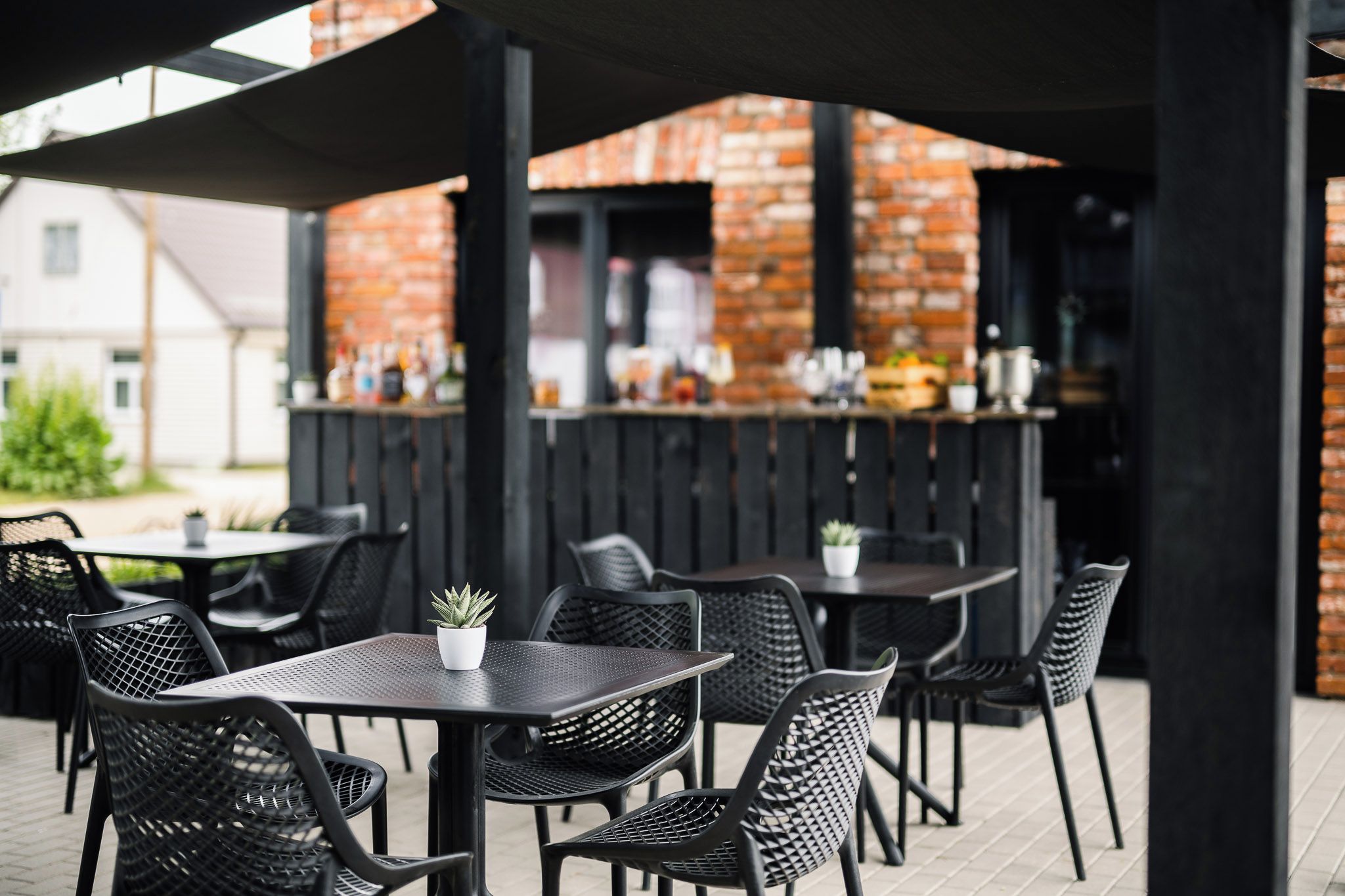 Un espace extérieur aménagé en terrasse, avec des tables et des chaises, un mur de briques en arrière-plan et un bar où divers articles sont exposés.