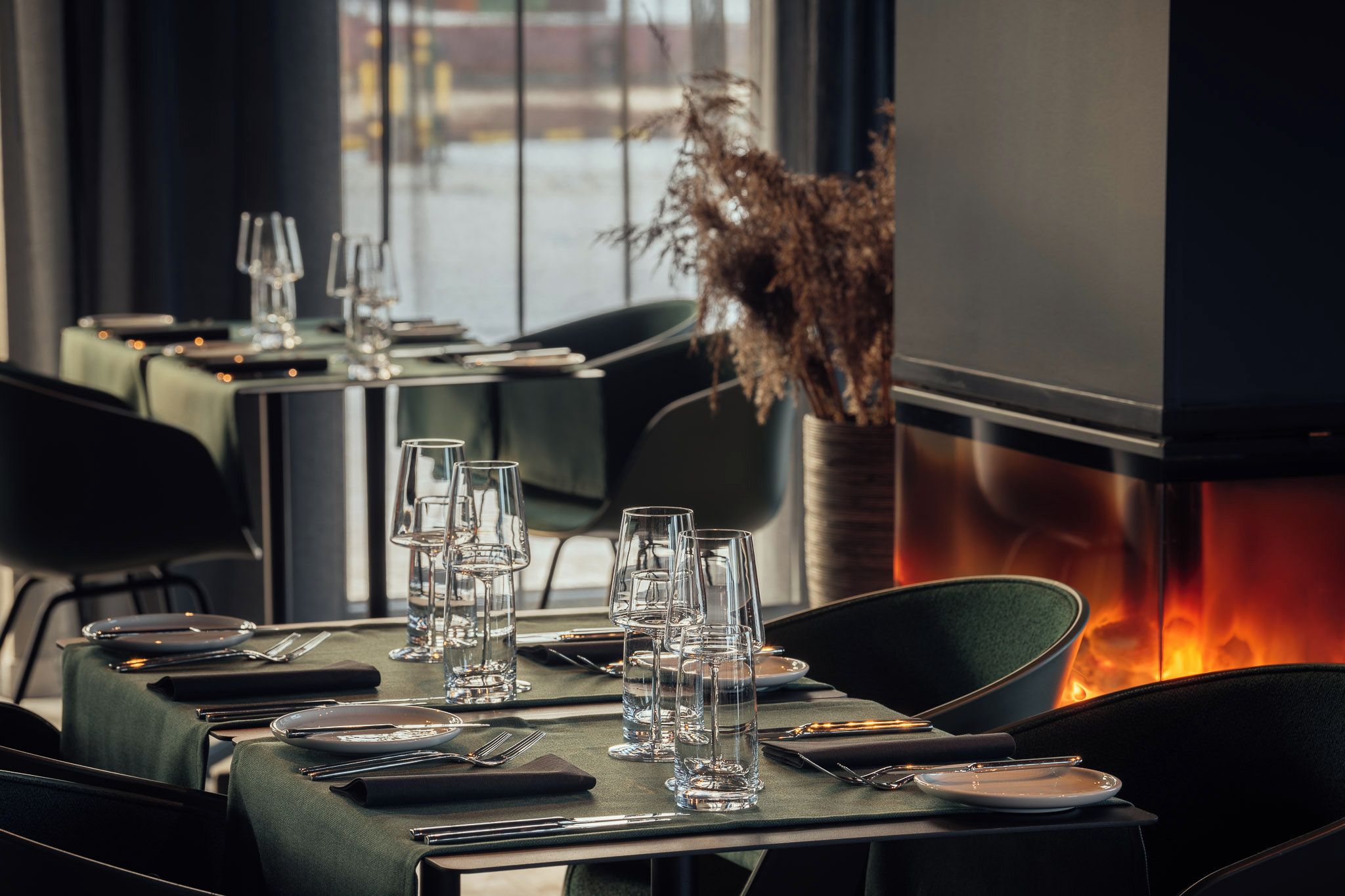 A restaurant interior with tables set for dining, clear glassware, and a decorative plant.