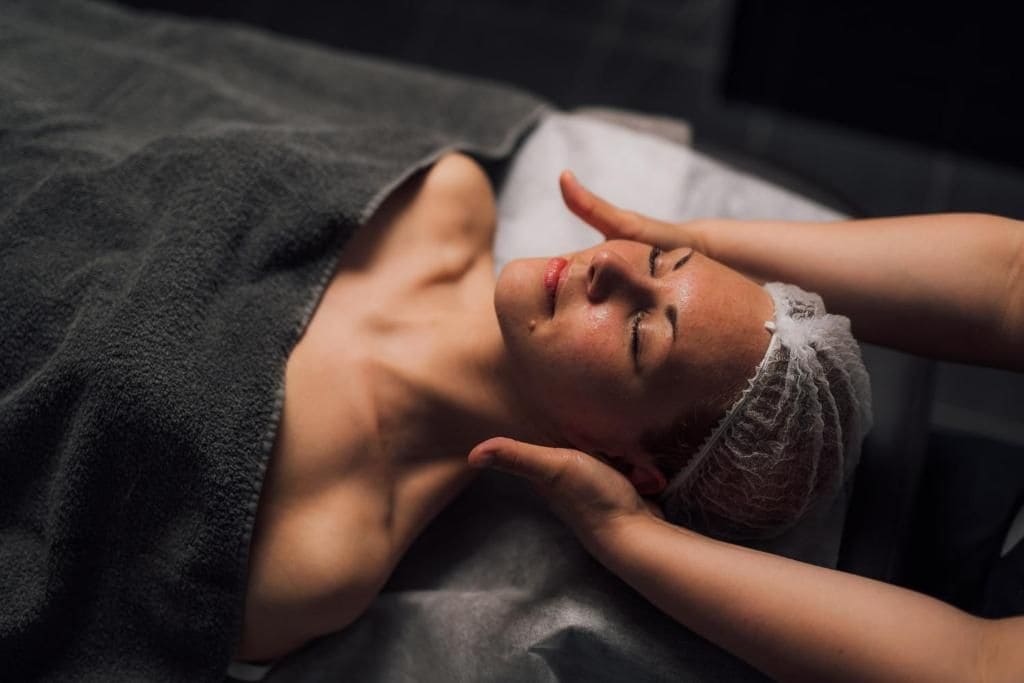 A person lying on a bed with a dark blanket, covered with a hairnet.