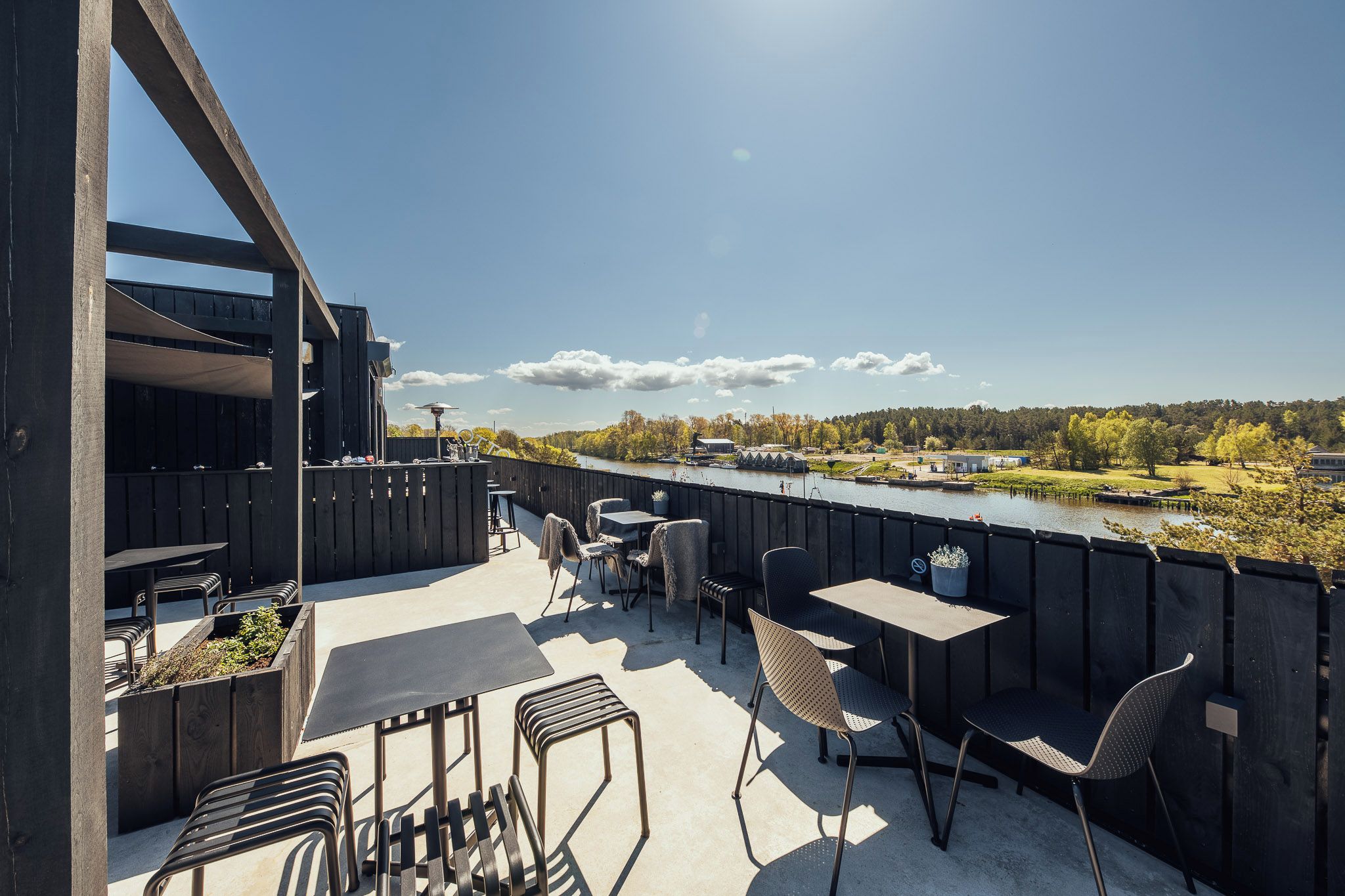 Een terras buiten met tafels en stoelen, met uitzicht op een rivier en een bebost gebied.