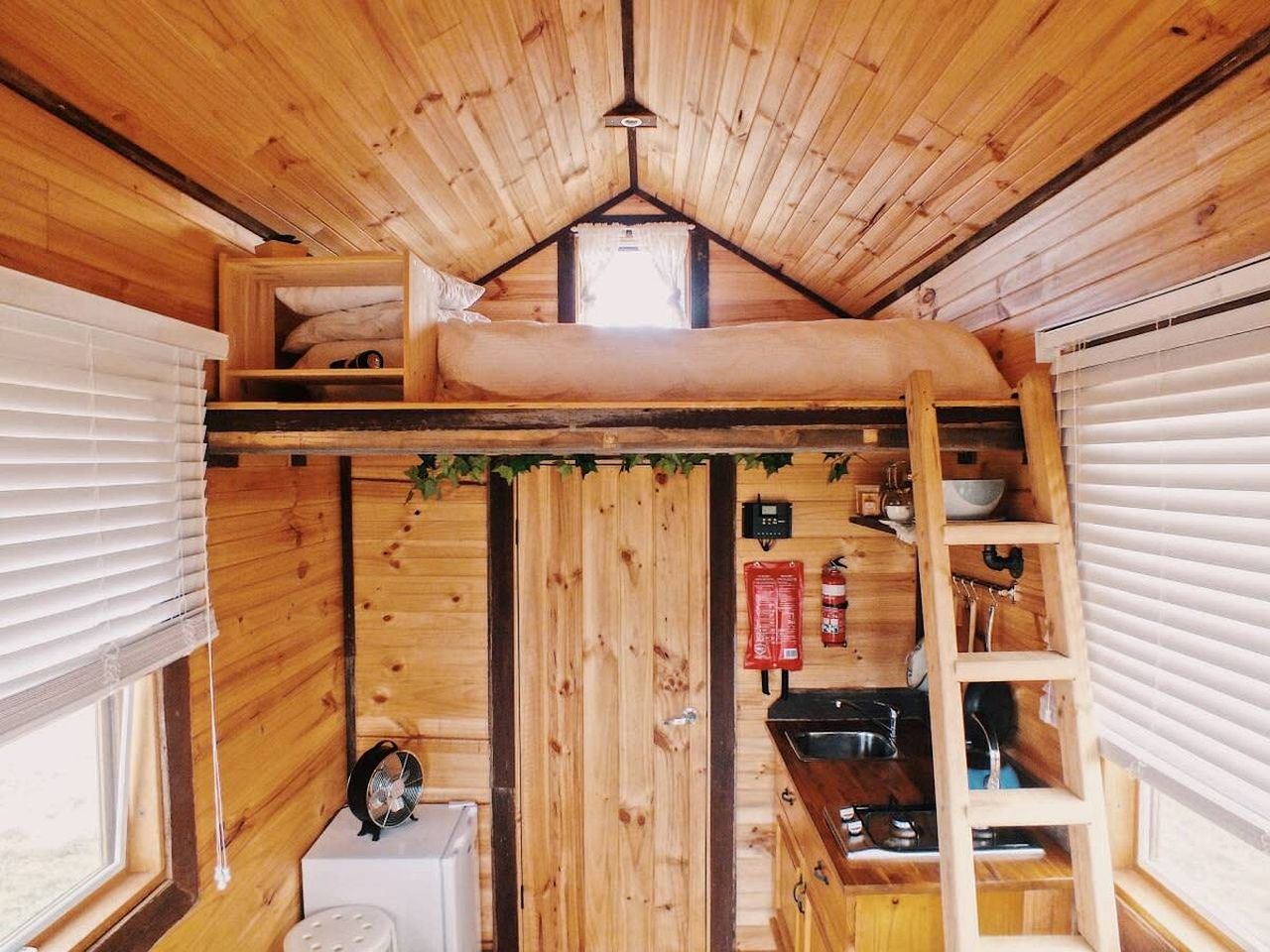 Un intérieur de cabine compact comprenant un lit en mezzanine, un coin cuisine et une petite salle de bain.