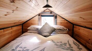 A small, cozy room with a sloped ceiling, a single bed with a floral-patterned bedspread, and a window at the far end.