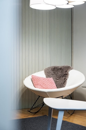 Ein modernes Zimmer mit einem weißen Stuhl, einem flauschigen grauen Kissen und einem rosafarbenen Kissen.