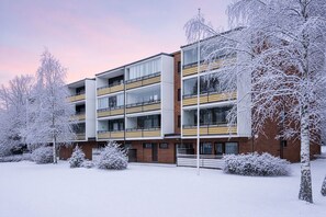 Ein mehrstöckiges Gebäude mit Balkonen, umgeben von schneebedeckten Bäumen und Sträuchern.