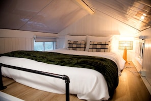 A bedroom with a bed, pillows, a bedside lamp, and a window.