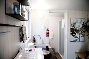 A bathroom with a sink, a mirror, a towel rack, a fire extinguisher, and a shower area.