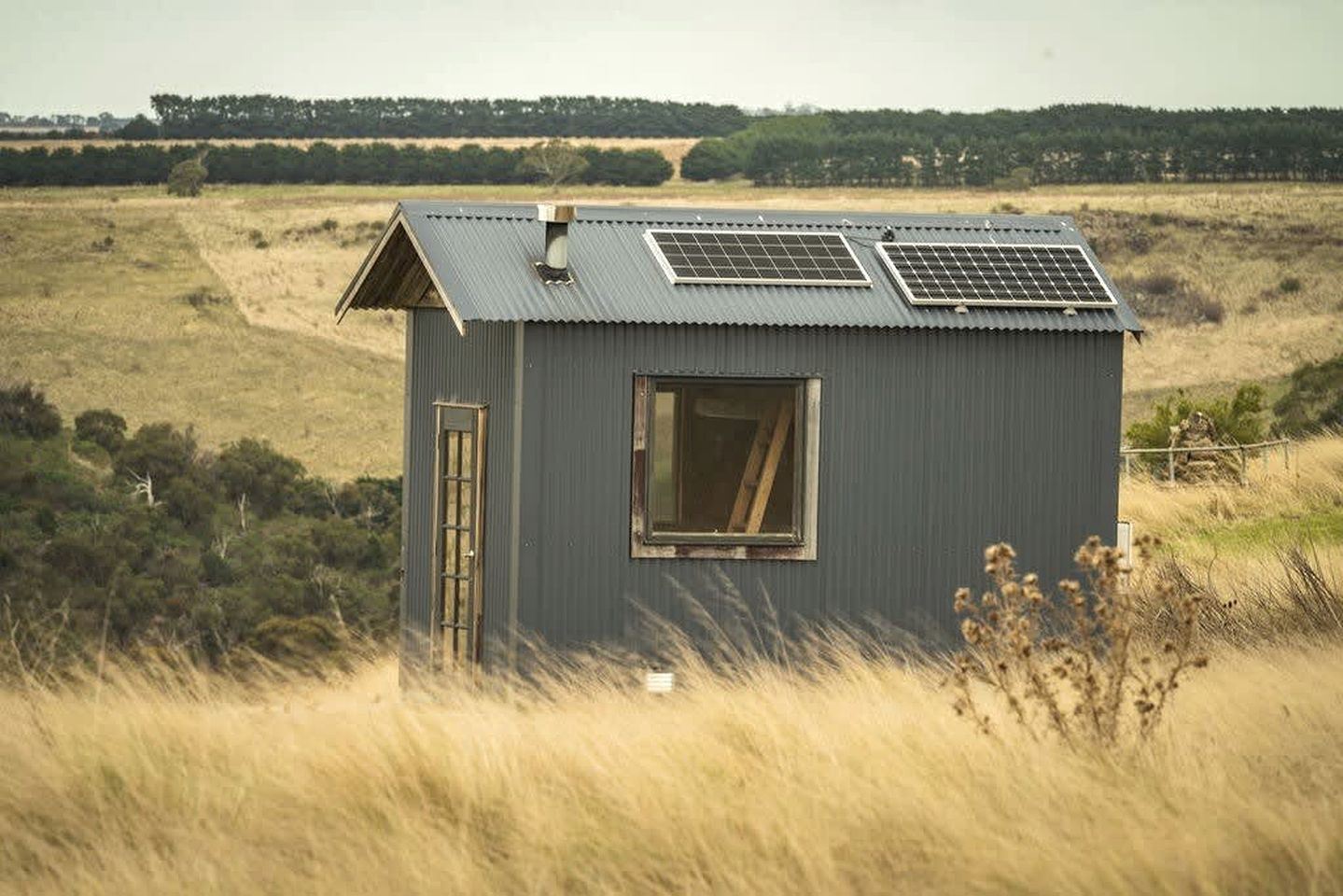 Um pequeno edifício térreo com telhado inclinado, uma janela e painéis solares no telhado.