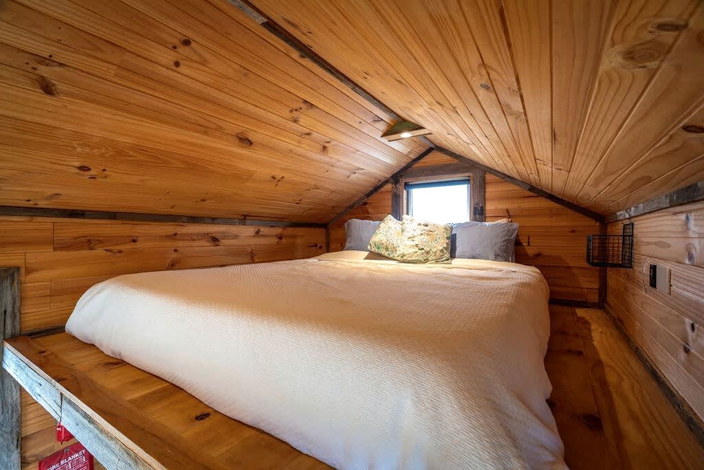 A cozy wooden cabin bedroom with a bed, pillows, and a window.