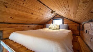 A cozy wooden cabin bedroom with a bed, pillows, and a window.