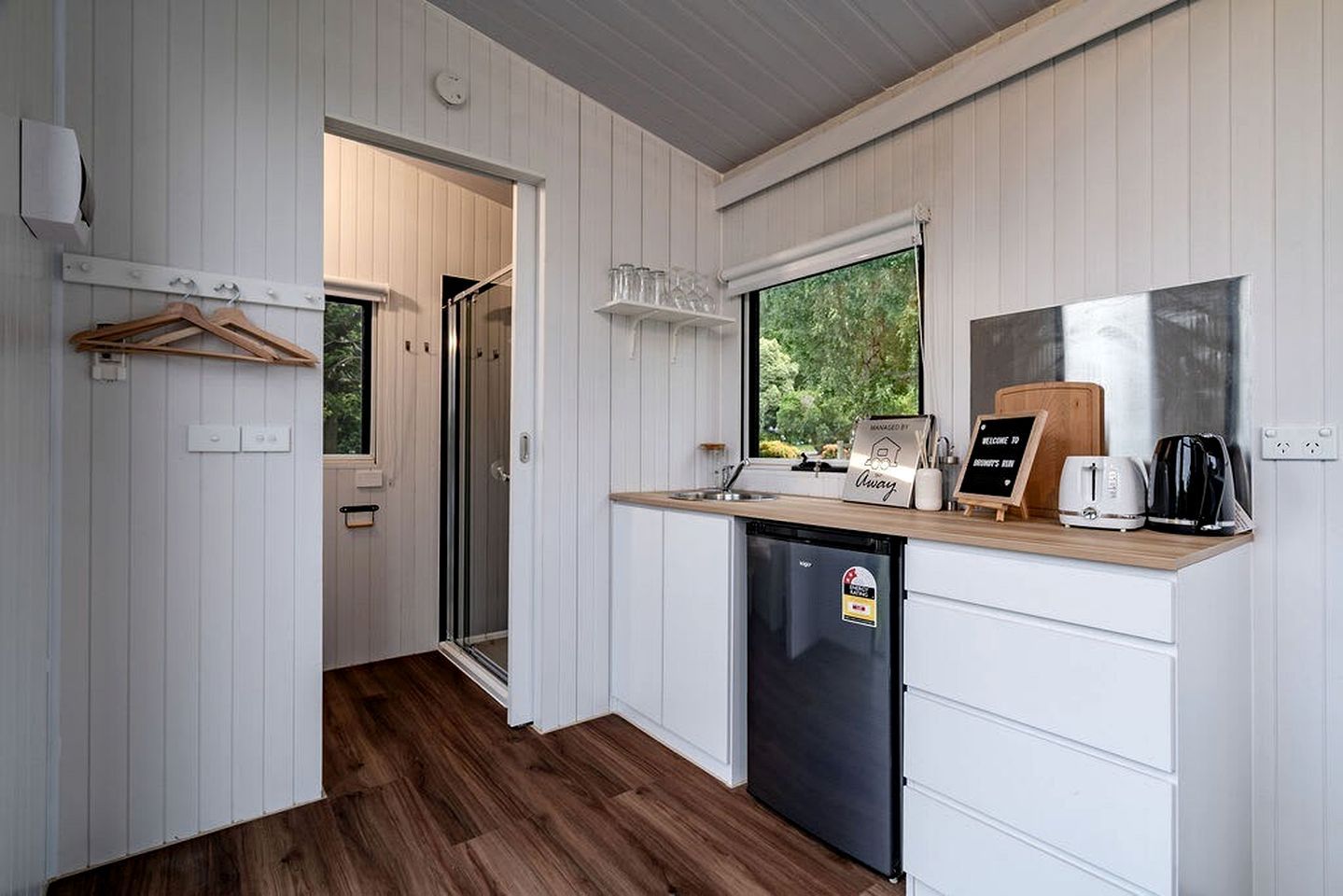 Une cuisine compacte équipée d’un lave-vaisselle, d’un plan de travail en bois et d’une fenêtre donnant sur un espace verdoyant.