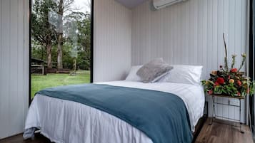 A bedroom with a bed, a window, an air conditioning unit, and a flower arrangement.