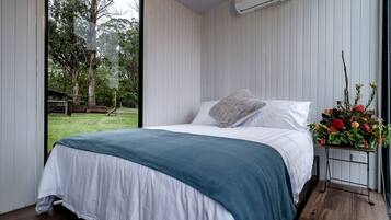 A bedroom with a bed, a window, an air conditioning unit, and a flower arrangement.