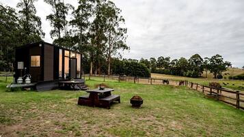 A modern cabin with a deck, surrounded by a fenced pasture with grazing animals.