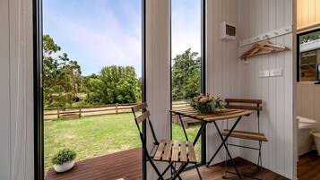 Een kamer met een houten tafel en stoelen, een kleine plant in een pot en uitzicht op een grasveld door grote ramen.