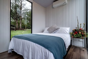 A bedroom with a bed, a window, an air conditioning unit, and a flower arrangement.