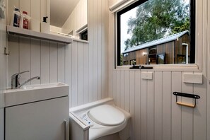 A bathroom with a window, a toilet, a sink, and a mirror.