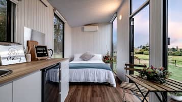 A bedroom with a bed, a small table, a bench, and a view of the outdoors.