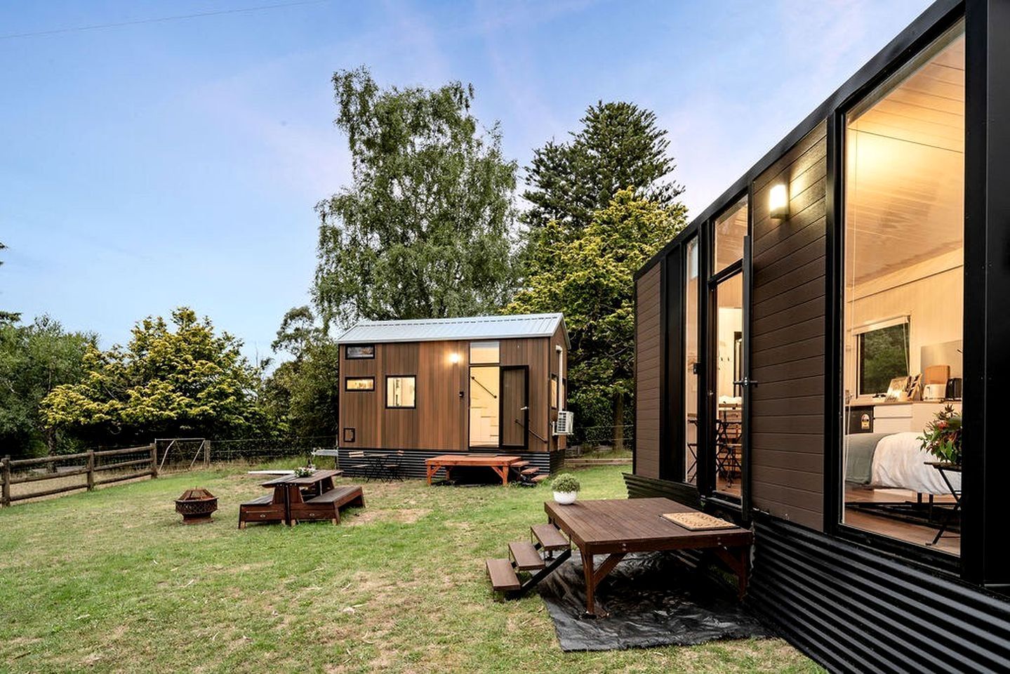A modern cabin with a wooden exterior, a patio area with a table and benches, and a large window.