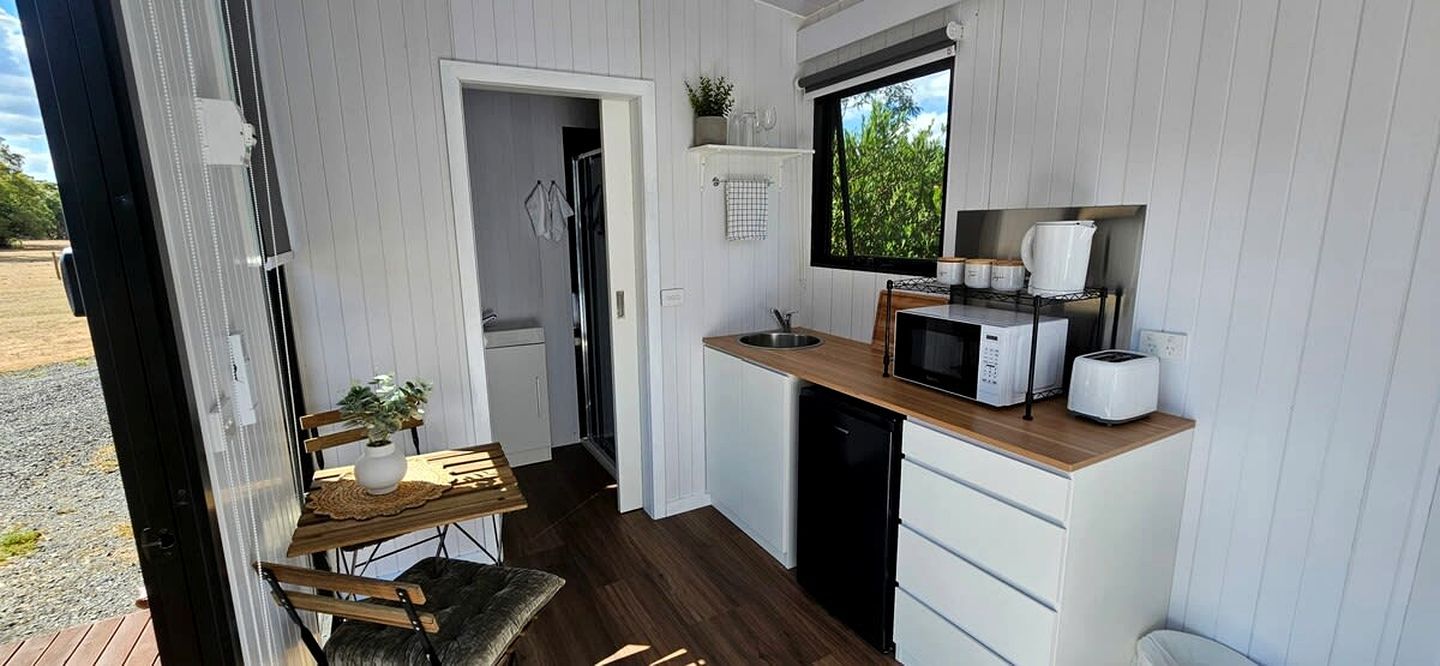 Een kleine keuken met een magnetron, gootsteen en een eethoekje met een tafel en stoel.
