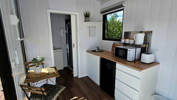 Een kleine keuken met een magnetron, gootsteen en een eethoekje met een tafel en stoel.