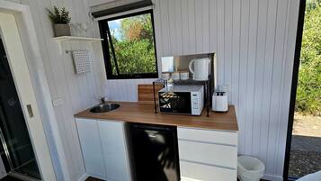 A compact kitchen with a sink, microwave, toaster, and a window with a view of greenery.