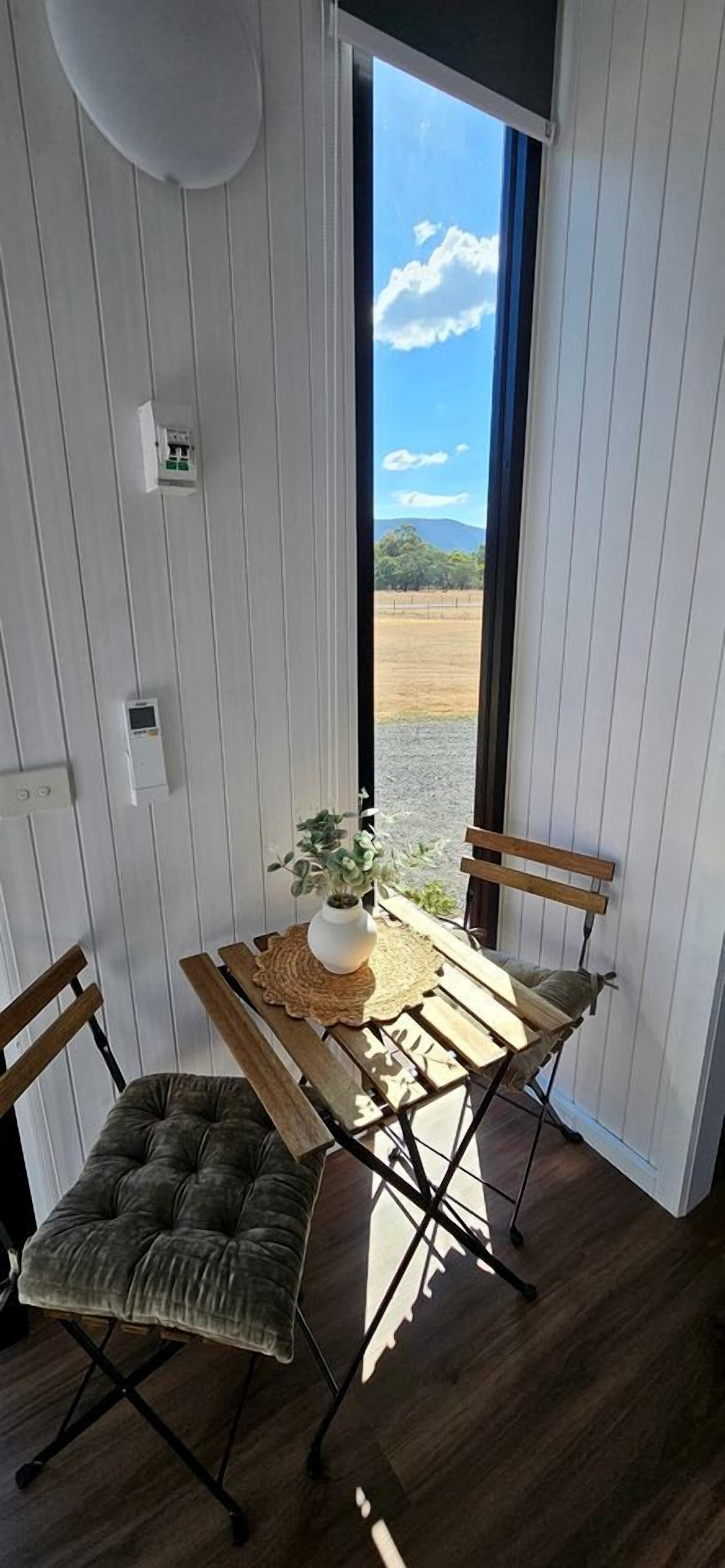 A room with a wooden table and two chairs, a plant on the table, and a view of the outdoors.