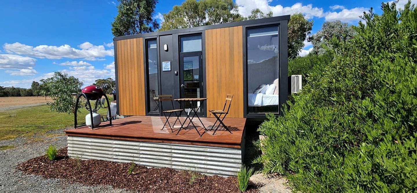 A modern, compact cabin with a deck, a bicycle, and a chair.