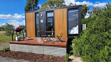 A modern, compact cabin with a deck, a bicycle, and a chair.