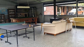 A room with a ping pong table, a sofa, a chair, a bookshelf, and a fireplace.