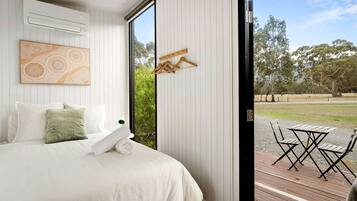A bedroom with a bed, a wall-mounted air conditioner, a wooden hanger, and a view of an outdoor area with a table and chairs.