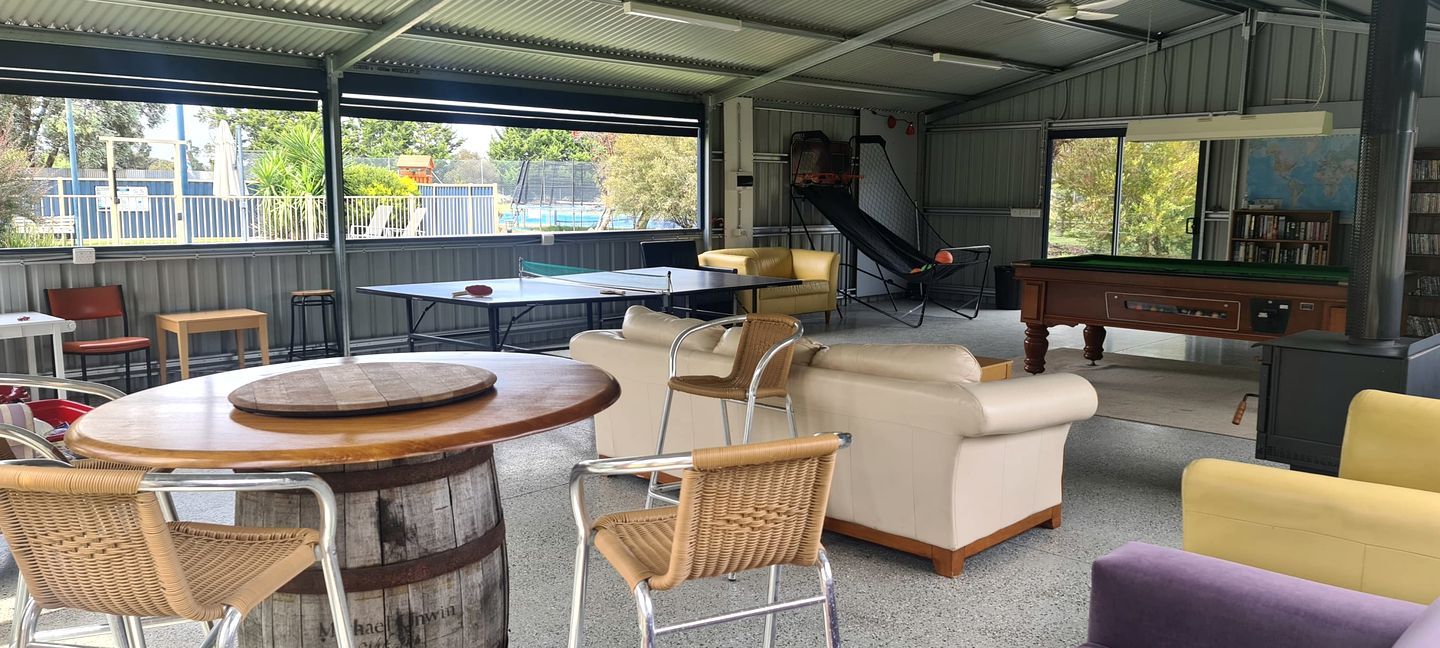 Un espacio recreativo interior con mesa de ping pong, mesa de billar y áreas de descanso que incluyen un sofá y sillas.
