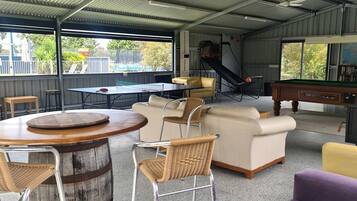 Un espacio recreativo interior con mesa de ping pong, mesa de billar y áreas de descanso que incluyen un sofá y sillas.