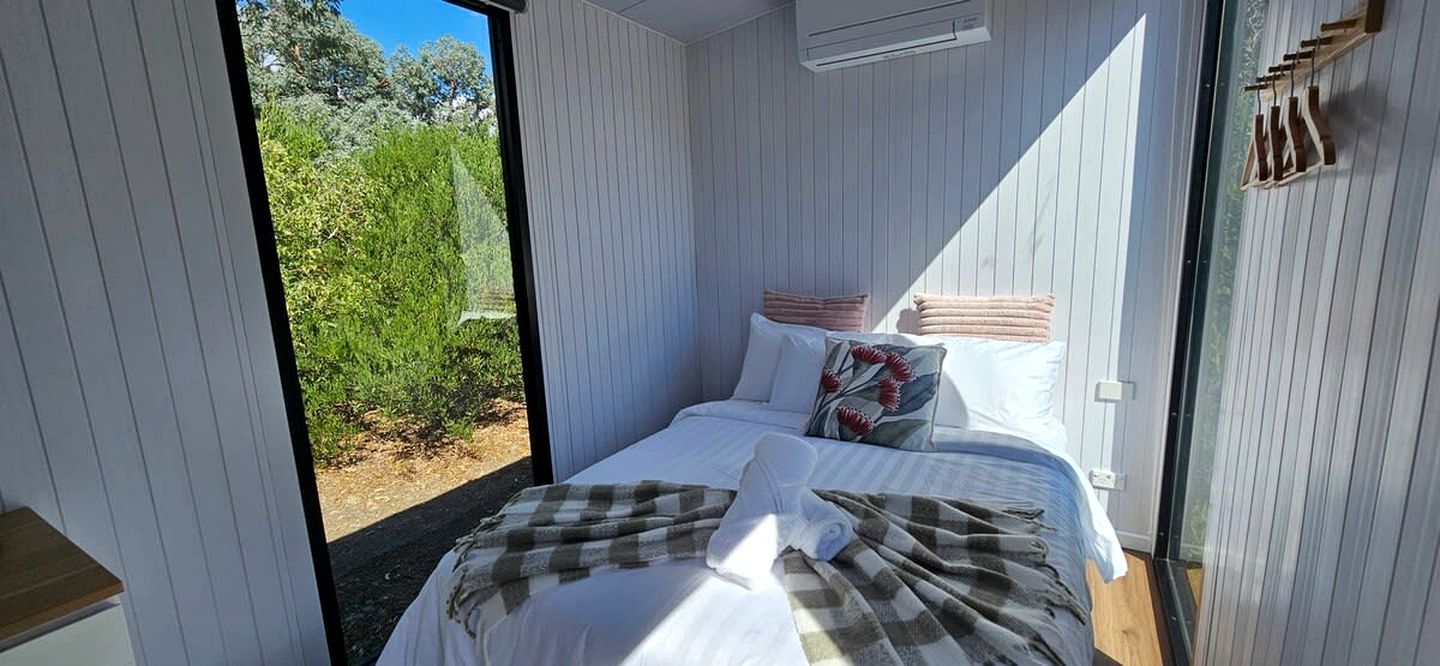 A bedroom with a bed, pillows, a blanket, and a view of greenery outside.