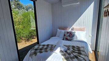 A bedroom with a bed, pillows, a blanket, and a view of greenery outside.
