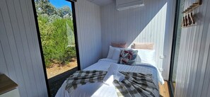 Un dormitorio con cama, almohadas, una colcha y vistas al verdor exterior.