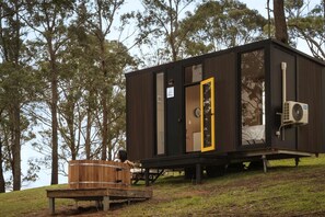 Una cabaña moderna con terraza de madera, puerta de vidrio y unidad de aire acondicionado.