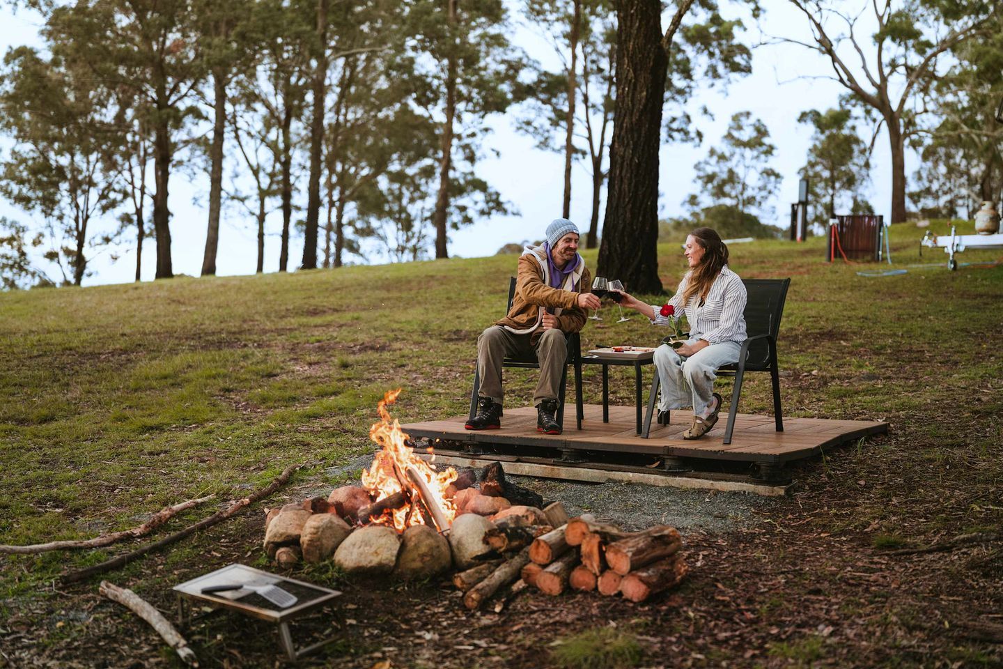 Two people seated at a table with a fire pit in the foreground.