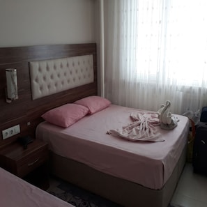A hotel room with a bed, a bedside table, a lamp, and a window with curtains.