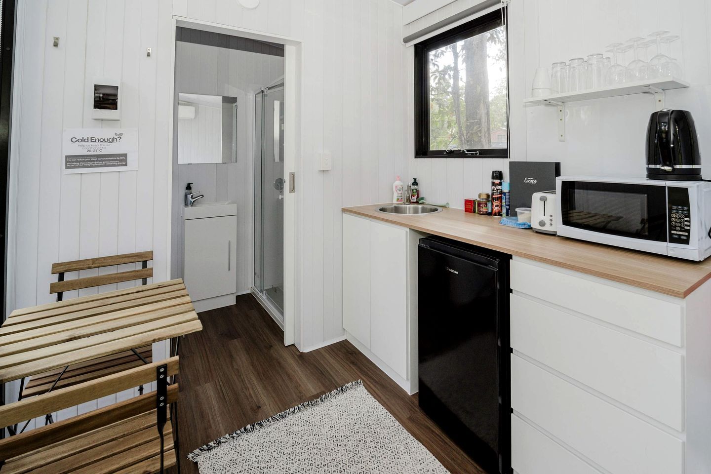Cozinha compacta com micro-ondas, torradeira e pia. Há um banco e um pequeno frigorífico.