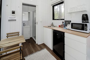Cozinha compacta com micro-ondas, torradeira e pia. Há um banco e um pequeno frigorífico.